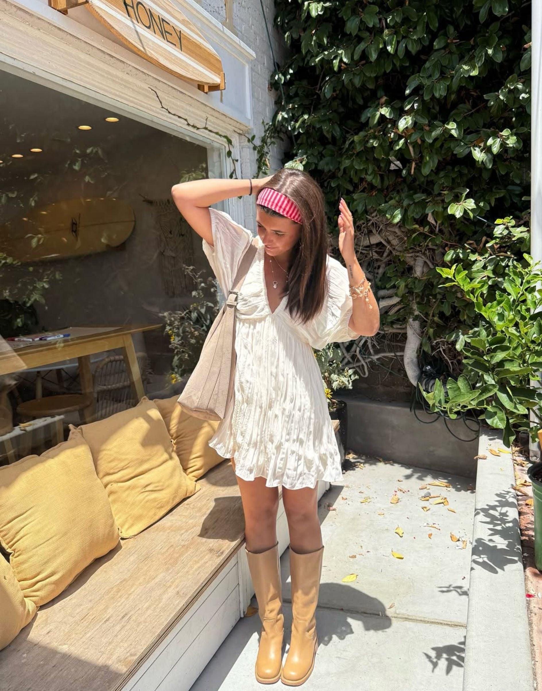 White summer mini dress styled with tan boots and a striped headband outside a sunny cafe.