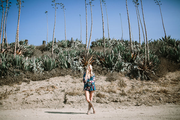 Teal floral romper as a summer vacation outfit, worn on sandy SoCal terrain lined with palms.