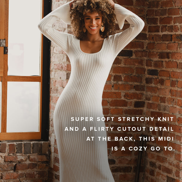 White ribbed knit midi dress with back cutout detail, shown against an exposed brick wall.