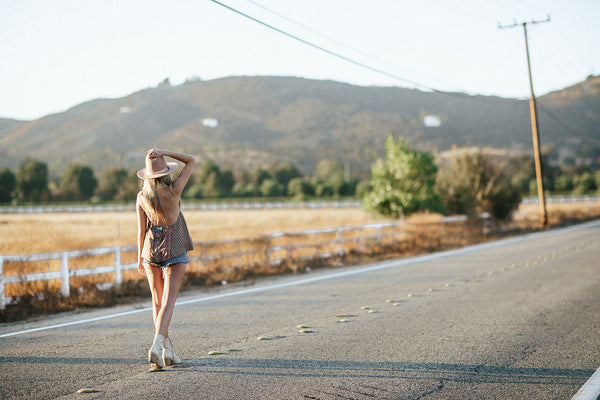 Woman in a bohemian festival outfit and sun hat on an open SoCal country road.