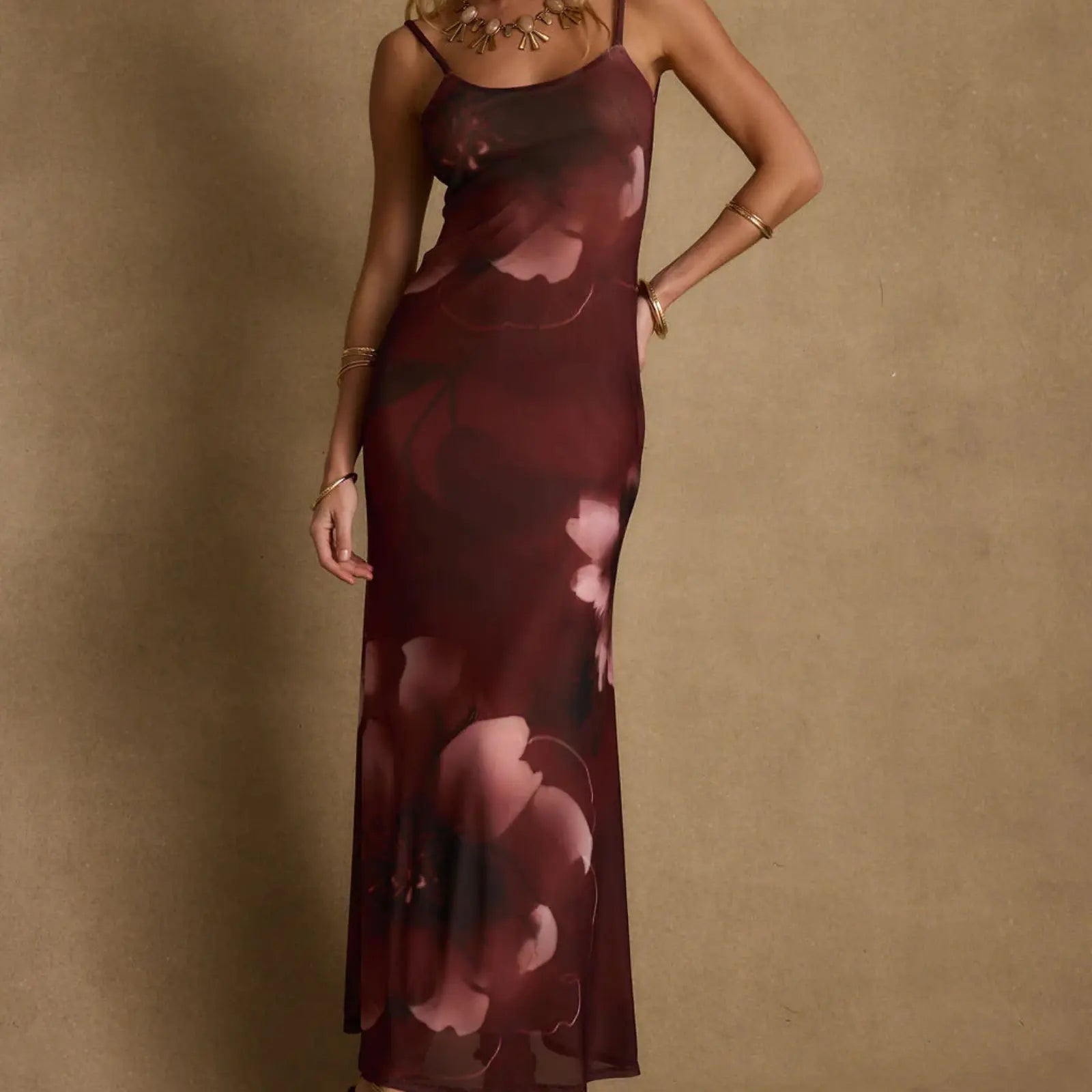 A deep burgundy floral-print slip maxi dress with spaghetti straps and gold jewelry, a sophisticated destination wedding wardrobe choice.