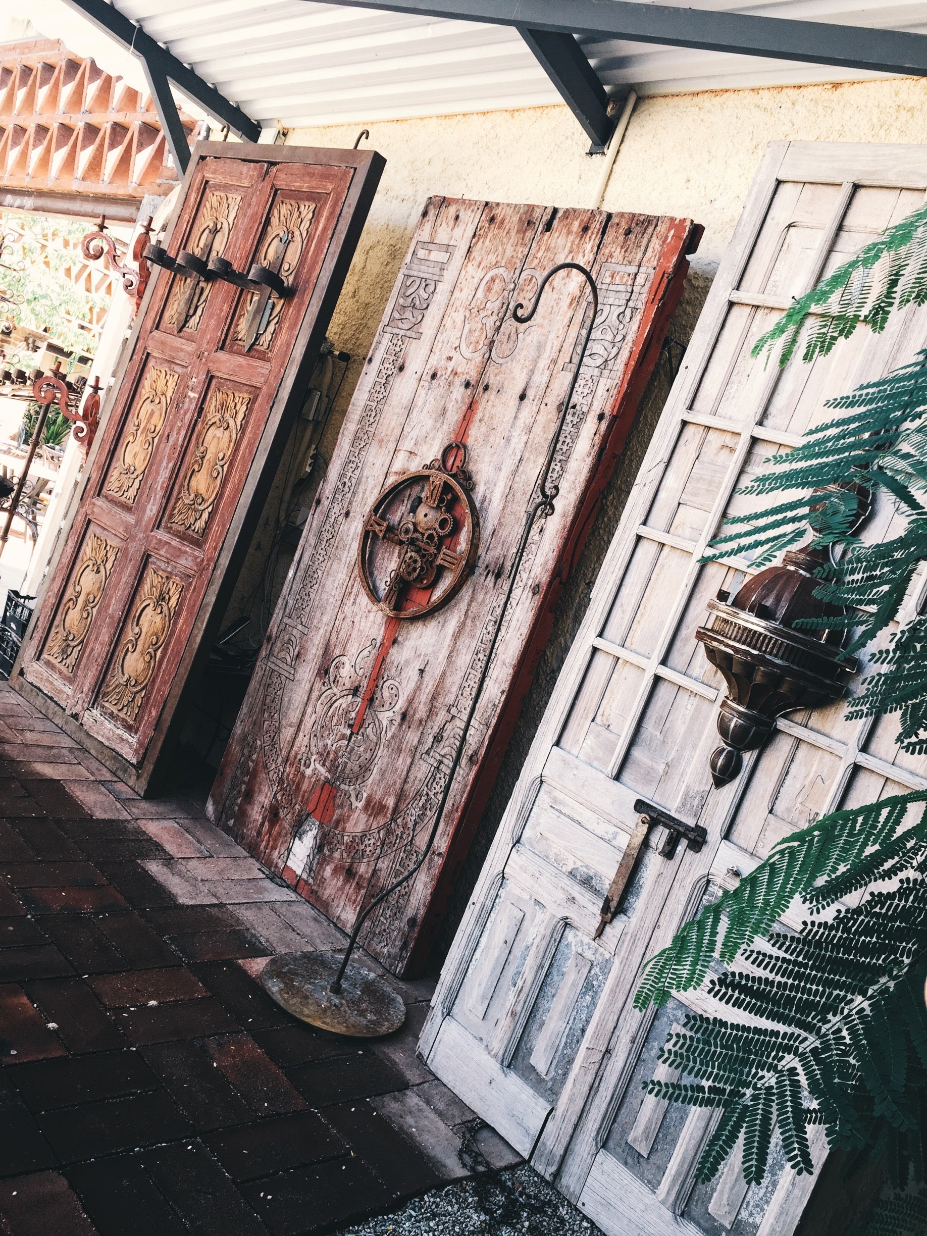 Carved antique wooden doors leaning against a stucco wall on a tiled patio.