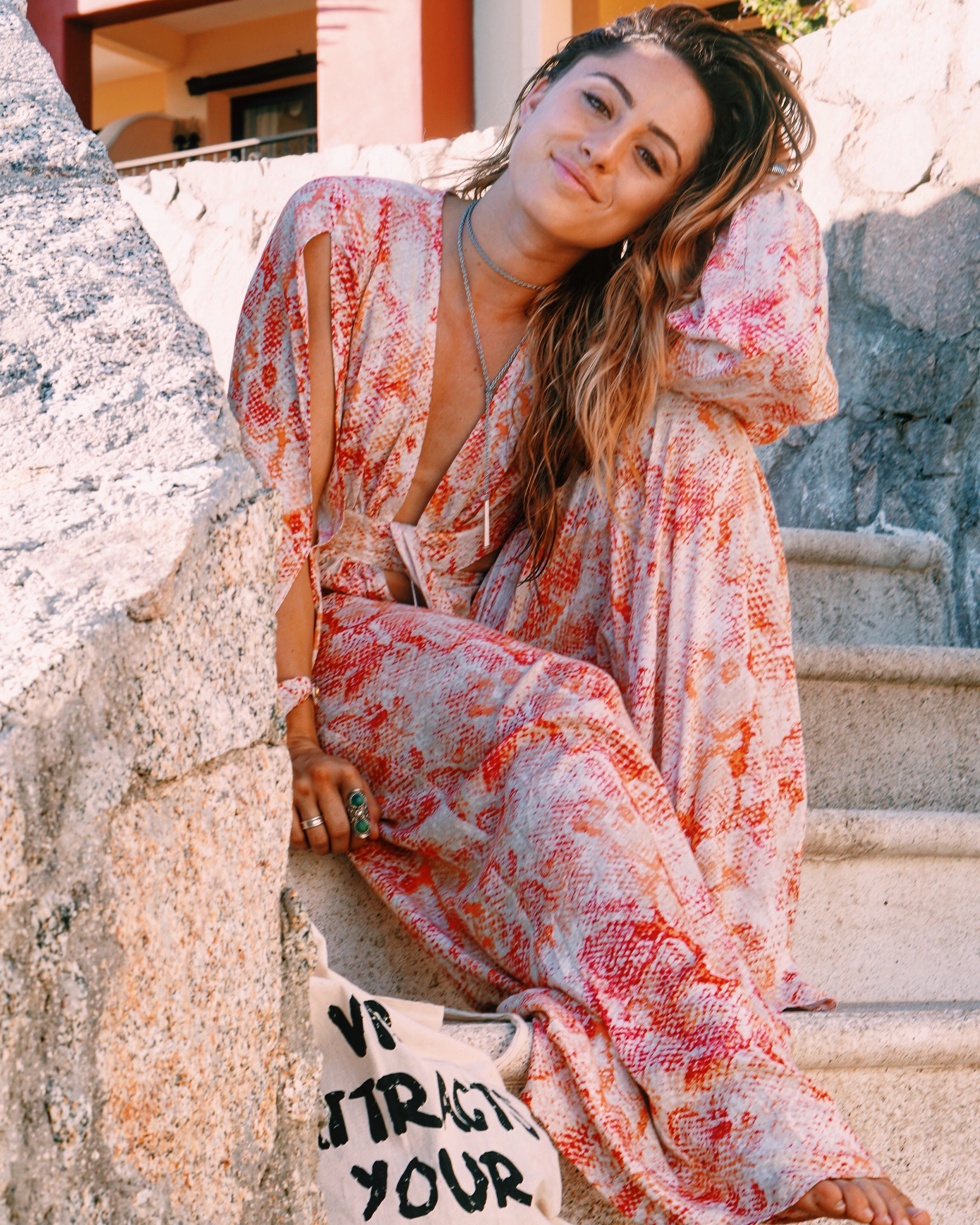 Woman in red and orange print maxi dress relaxing on sunlit resort steps.