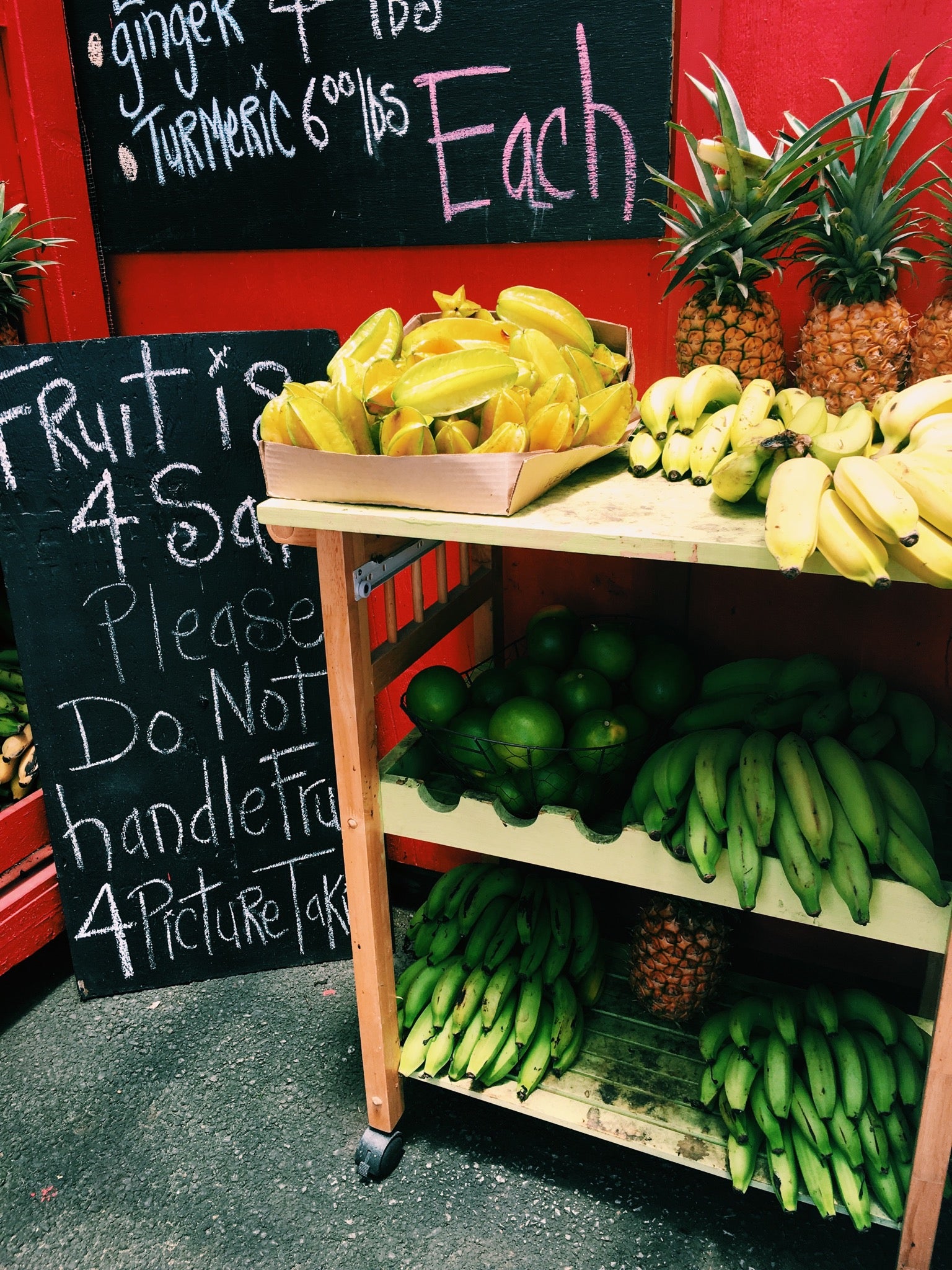 Roadside fruit stand in Kauai with starfruit, bananas, pineapples and chalkboard price signs.
