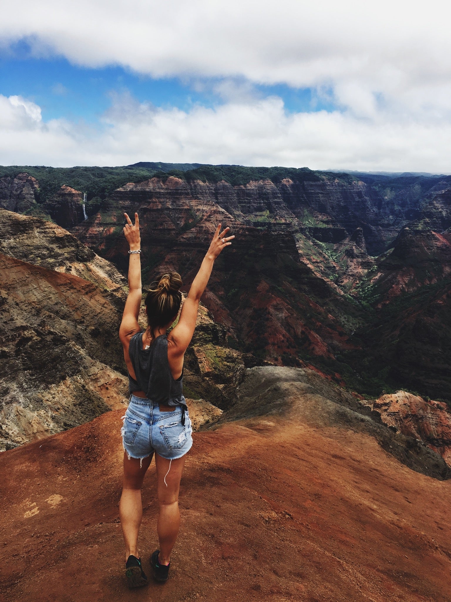 Person with arms raised in peace signs overlooking the red cliffs of Waimea Canyon, Kauai.