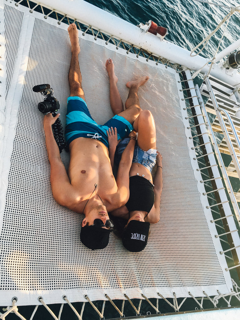 Couple lounging on a catamaran trampoline net above clear water during a tropical getaway.