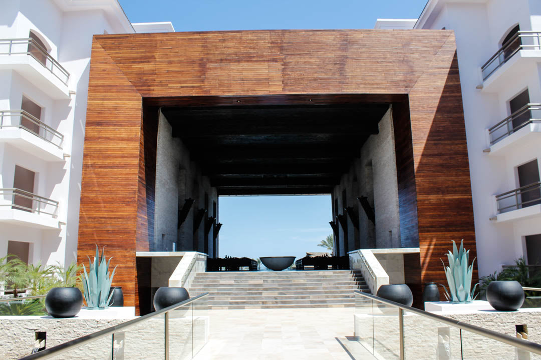 Wood-framed resort entrance at Cabo Azul, framing ocean views beyond a stone staircase in Cabo San Lucas.