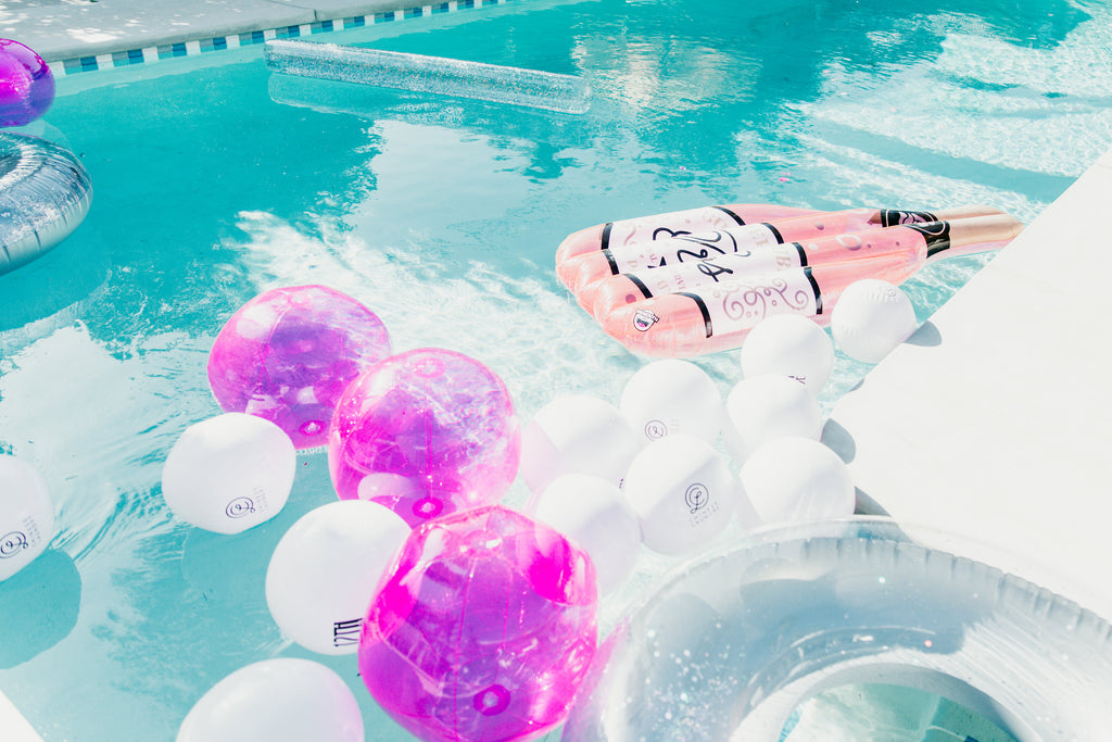 Rosé bottle pool float drifting among pink and white beach balls at a Coachella pool party.