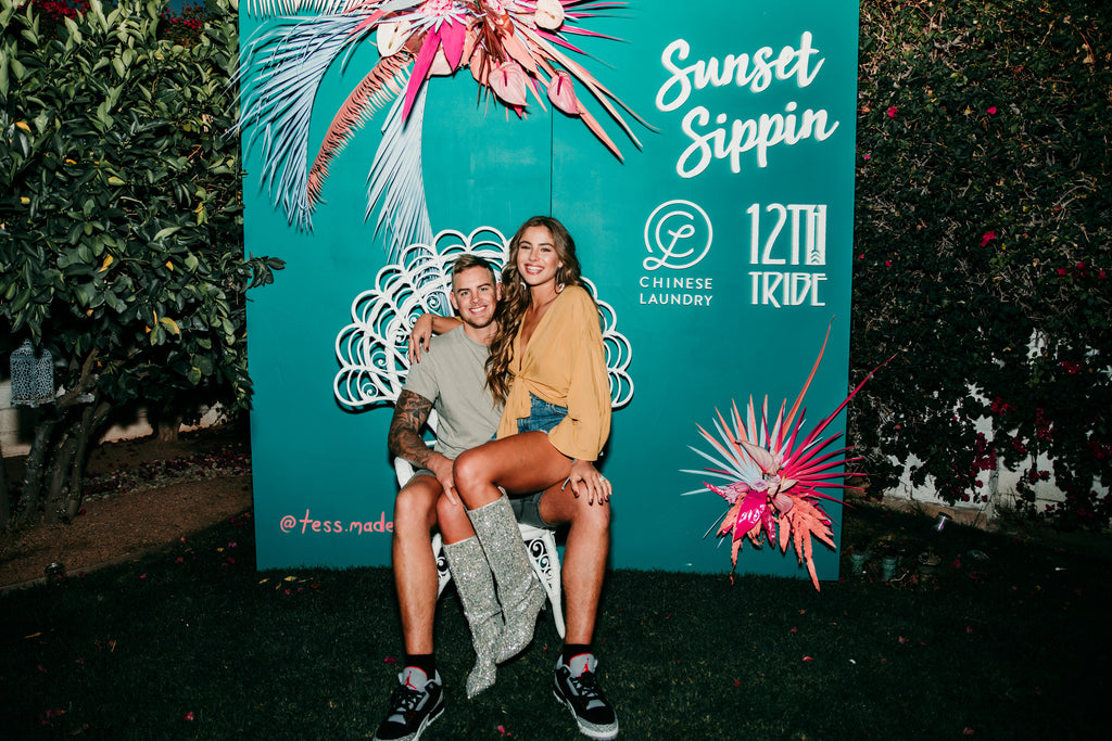 Couple posing at the Sunset Sippin Coachella event, woman in yellow festival wrap top.