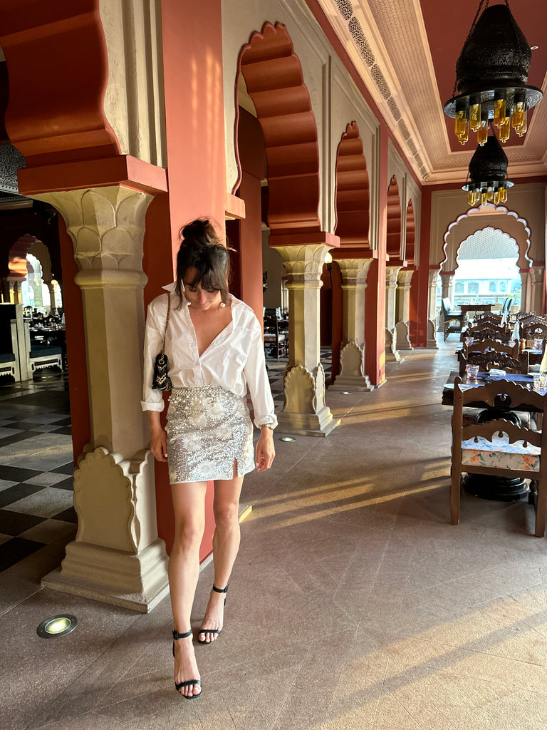Woman in white shirt and beaded mini skirt walking through an ornate Indian palace corridor.