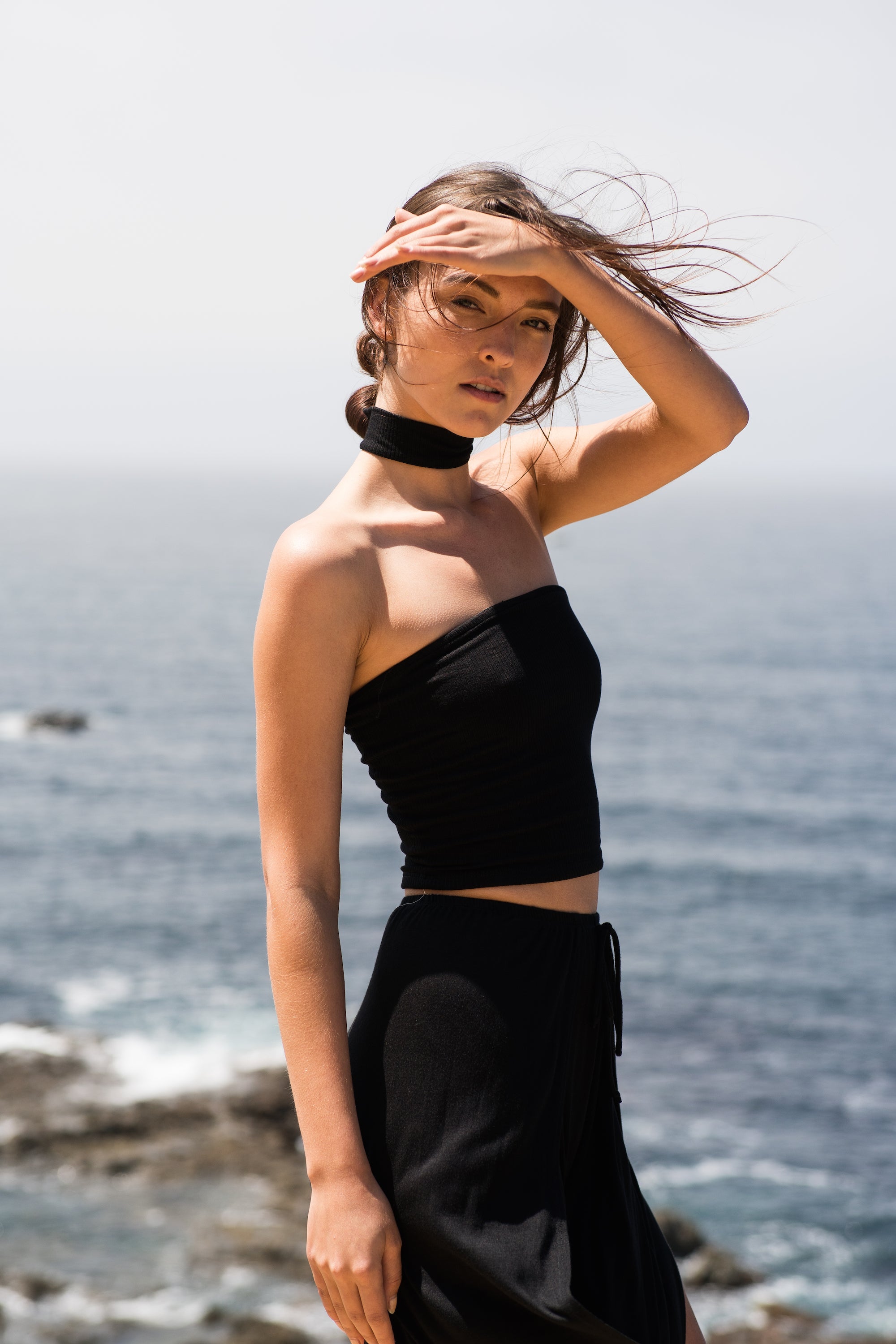 Model in a black strapless top and skirt posing on a rocky coastline.
