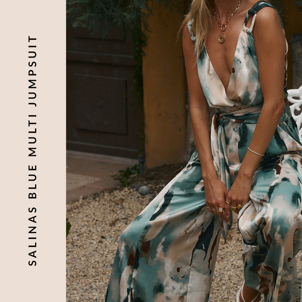 Flowing watercolor Salinas blue jumpsuit styled as a resort outfit for women in an Italian courtyard.