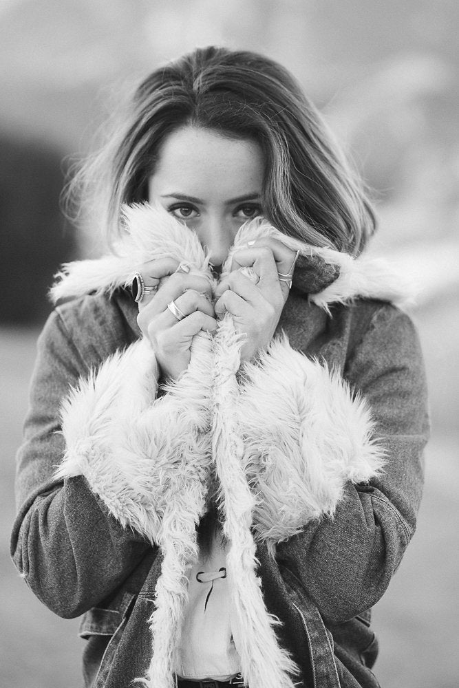 Black and white portrait of a woman clutching a fur-lined denim jacket to her face.