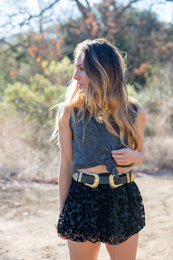 Boho festival outfit with grey knotted tank, black floral shorts, and gold double-buckle belt.