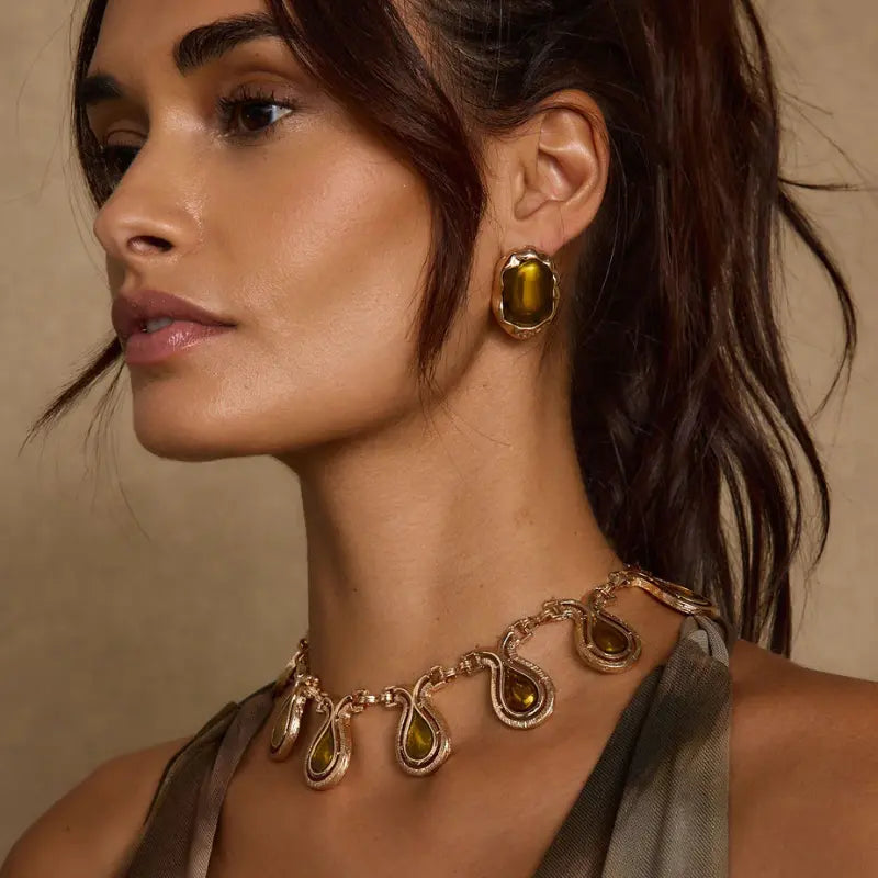 Accessories for a maxi dress including gold snake-motif teardrop statement necklace with amber stones and matching oversized stud earrings paired with a satin olive gown