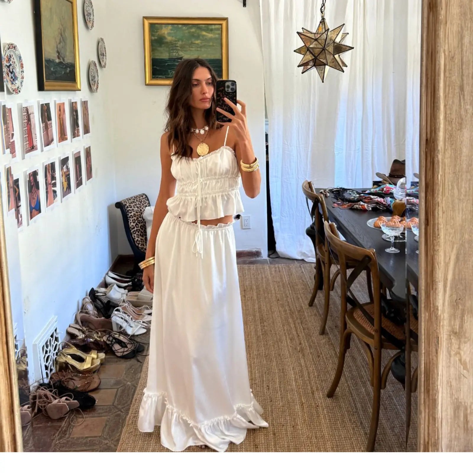 A mirror selfie of a woman in a white ruffled crop top and satin maxi skirt with gold coin jewelry, showcasing an elegant dress co-ord for summer.