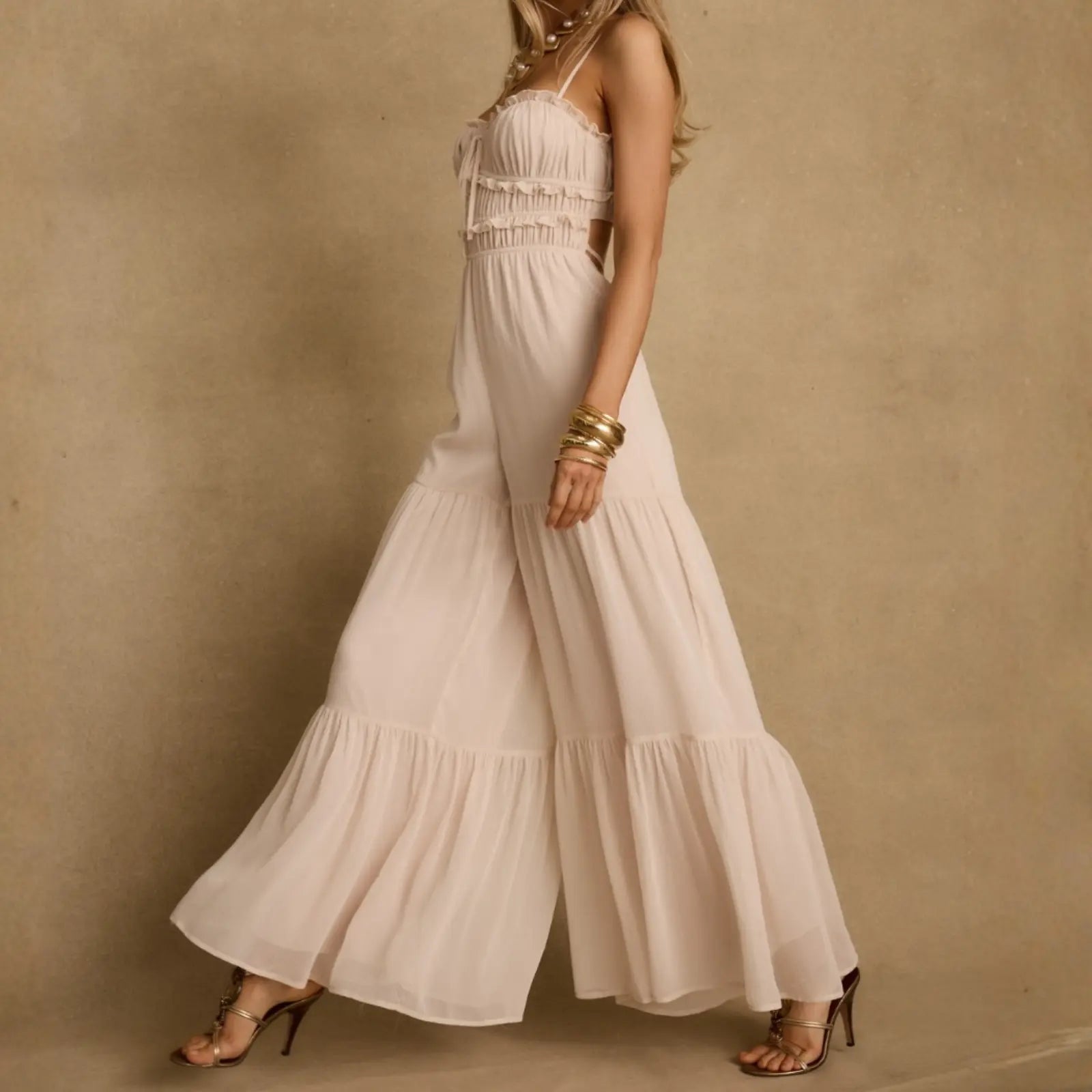 A flowing blush wide-leg jumpsuit with ruffle details and gold accessories, a elegant take on summer resort wear styled with strappy heels.