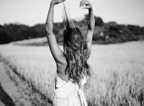 Black and white photo of a person facing a sunlit field, arms raised in denim overalls.