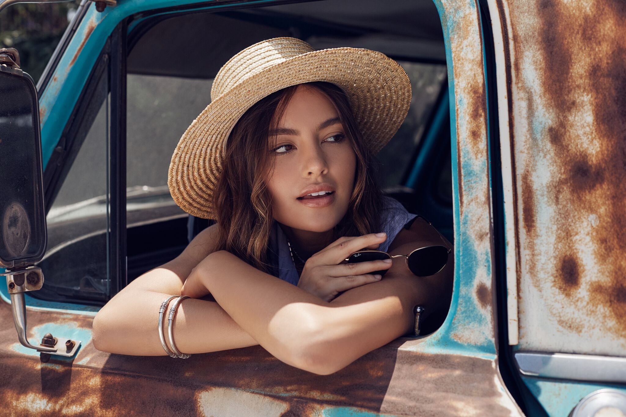 Model in a straw boater hat leaning out a vintage rusted turquoise truck window.